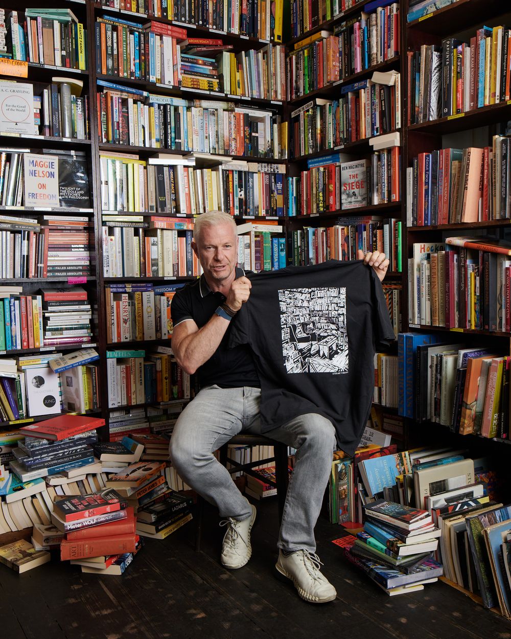 David Francis seated in a bookshop, surrounded by floor-to-ceiling shelves
