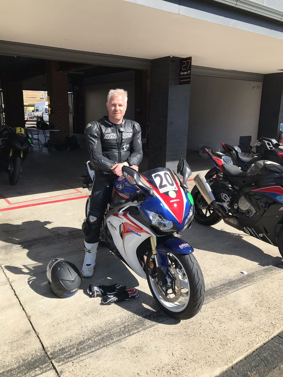 David Francis in racing leathers leaning on a sports motorbike in a pit garage